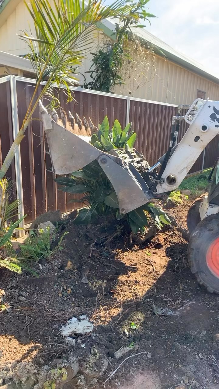 Skid-steer loader digging and moving soil beside a corrugated fence
