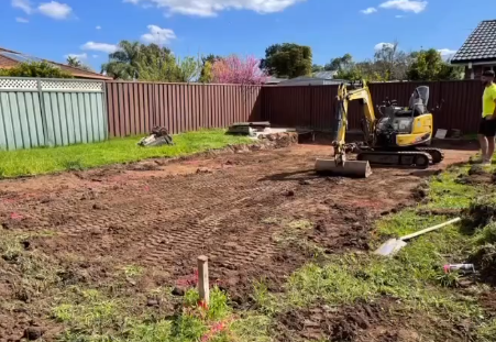 Mini excavator clearing and stripping topsoil in a backyard ahead of outdoor works